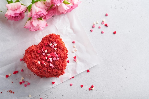 Zwei Kuchen Roter Samt in Form von Herzen auf weißem Teller Rosenblüten und Tasse Kaffee auf rosa romantischem Hintergrund Dessert-Idee für Valentinstag, Muttertag oder Frauentag Leckeres hausgemachtes Dessert