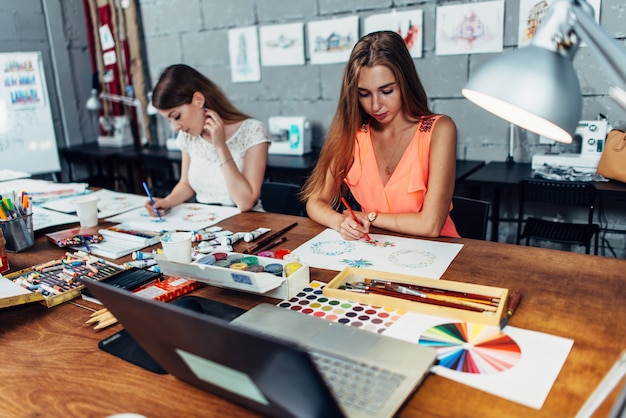 Zwei Künstlerinnen, die dekorative Elemente zeichnen, die am Schreibtisch im kreativen Studio sitzen