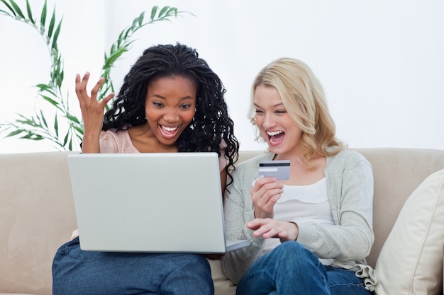 Zwei lachende Frauen mit einem Laptop und einer Bankkarte