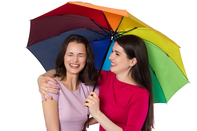 Zwei lachende junge Frauen mit Regenbogenregenschirm.