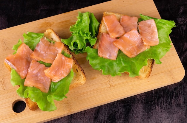 Zwei Lachsbrötchen auf hellem Holzbrett, Draufsicht.