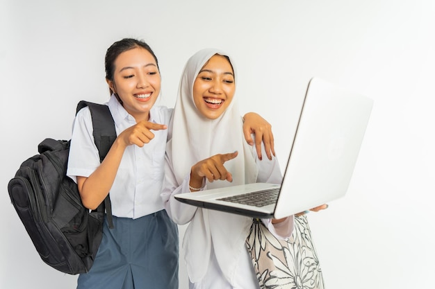 Zwei lächelnde Berufsschülerinnen tragen Taschen, während sie einen Laptop auf weißem Hintergrund benutzen