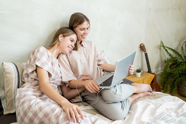 Zwei lächelnde, erholsame Mädchen mit Laptop, die einen Film ansehen