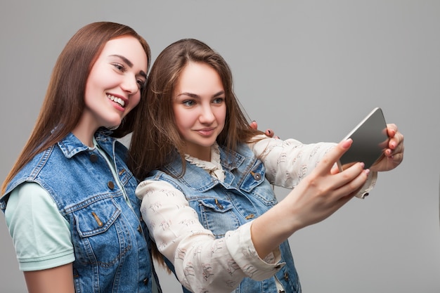 Zwei lächelnde freundinnen in jeansjacken machen selfie auf telefonkamera