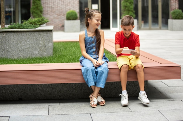 Zwei lächelnde Kinder, Junge und Mädchen, die zusammen Smartphone in der Stadt am Sommertag spielen