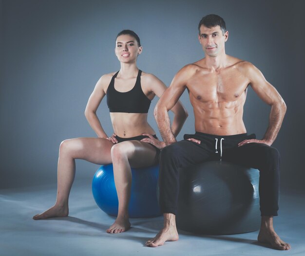 Foto zwei lächelnde leute mit fitnessball in der turnhalle. persönlicher fitnesstrainer. personal training. fitnesstraining.