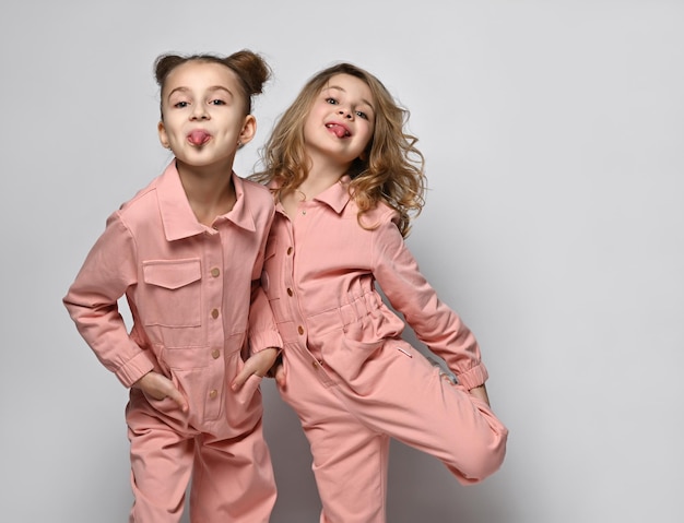 Zwei lächelnde Mädchen Freundinnen Schwestern in rosafarbenen Baumwolloveralls mit Taschen stehen dicht beieinander