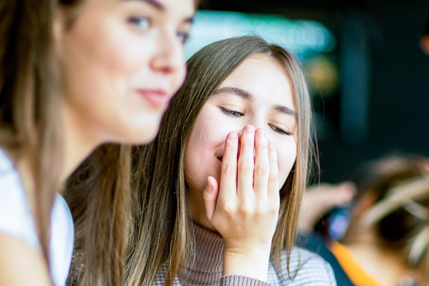 Zwei lächelnde Mädchen unterhalten sich und schließen den Mund mit der Hand