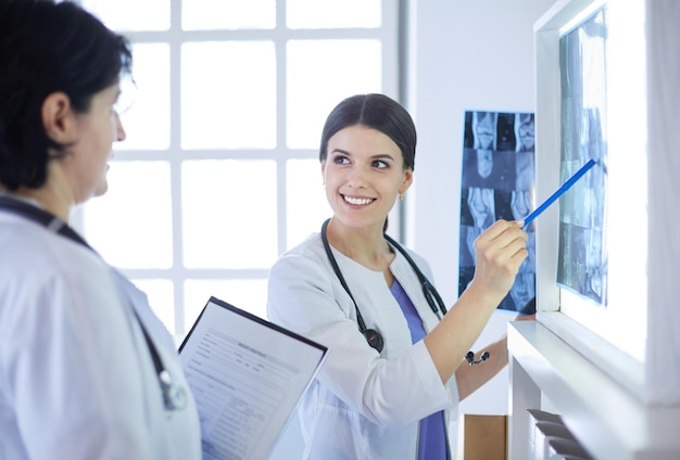 Zwei lächelnde Ärzte, die auf Röntgenbilder in einem Sprechzimmer eines Krankenhauses zeigen