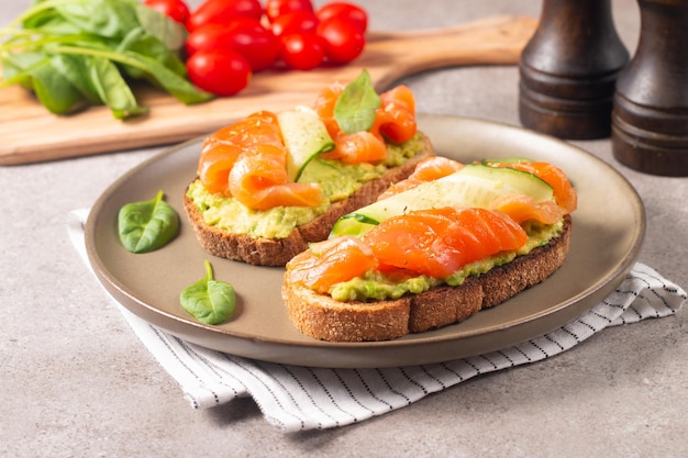 Zwei leckere offene Lachssandwiches mit Avocado und Gurke. Gesundes Frühstück am Morgen. Ansicht von oben.