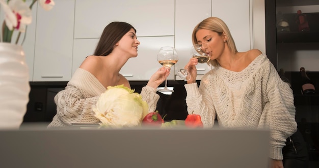 Zwei lesbische Freundinnen machen Salat in der Küche und trinken Wein aus Weingläsern