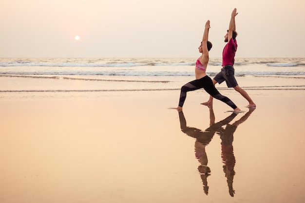 Zwei Leute, die Yoga im Abendlicht am Strand von Goa Indien praktizieren. weibliche und männliche Acro Yogi Tantra Flying Copyspce.