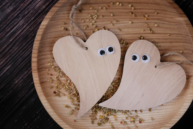 Zwei lustige Holzherzen mit Augen auf einer Holzplatte auf einem hölzernen Hintergrund. Karte zum Valentinstag.