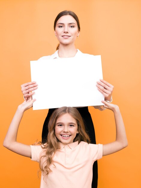 Foto zwei lustige mädchen, die ein durchsichtiges blatt papier auf orangefarbenem hintergrund halten, verspotten sich