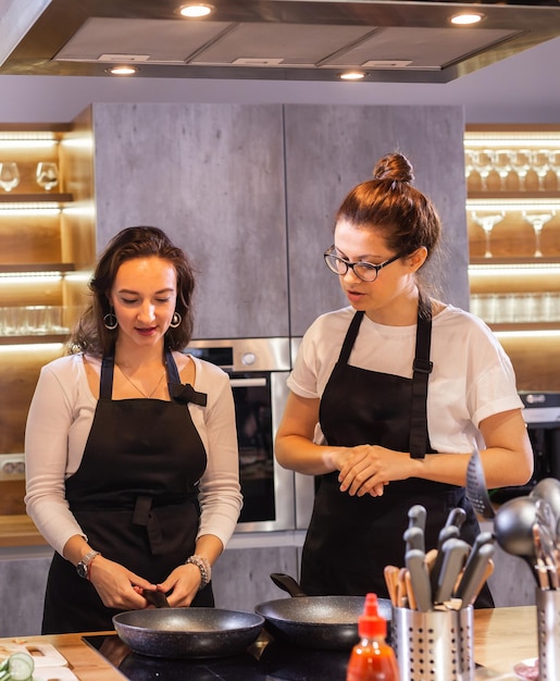 Zwei lustige professionelle Köchinnen kochen Essen in einer großen Küche