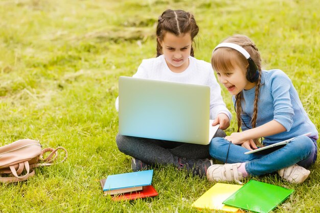 Zwei lustige Schulmädchen sitzen im Gras und lesen Bücher. Mädchen, Freundinnen, Schwestern werden in der Natur unterrichtet.