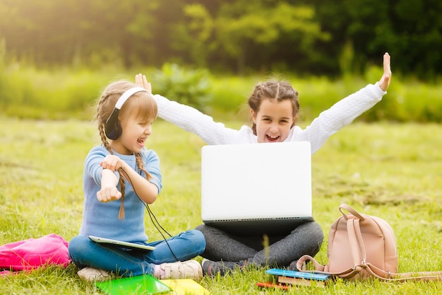 Zwei lustige Schulmädchen sitzen im Gras und lesen Bücher. Mädchen, Freundinnen, Schwestern werden in der Natur unterrichtet.