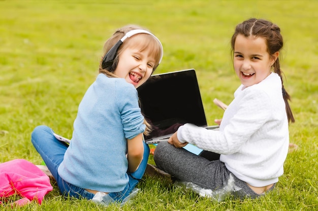 Zwei lustige Schulmädchen sitzen im Gras und lesen Bücher. Mädchen, Freundinnen, Schwestern werden in der Natur unterrichtet.