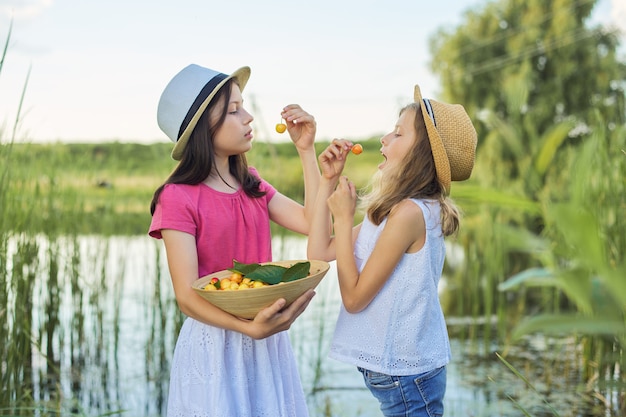Zwei Mädchen, die gelbe Kirschen in der Natur essen