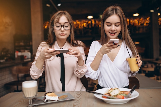 Zwei Mädchen, die in einem Café zu Mittag essen und Fotos machen