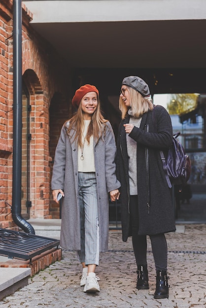 Zwei Mädchen, die zusammen auf der Straße gehen und ihre Hände halten, tragen sie Frühling oder Herbst