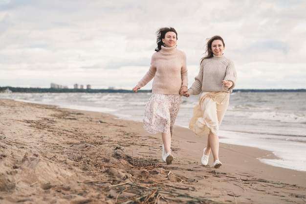 Zwei Mädchen halten Händchen und laufen am Meer entlang, die Schwestern haben Spaß zusammen mit einem verliebten Paar auf einem ...