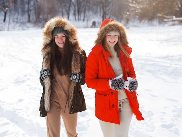 Zwei Mädchen im Winter, in warmer Kleidung, den Schnee genießend, im Freien. Kalte Jahreszeit, Lachen und Spaß. Winterwald, weiße Lichtung.