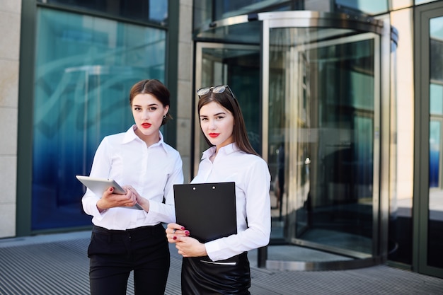 Zwei Mädchen in der Geschäftskleidung auf dem Hintergrund eines Bürogebäudes