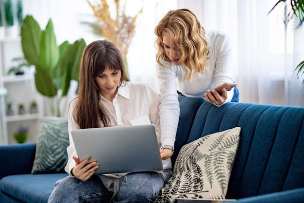 Zwei Mädchen in Hemden besprechen etwas, während sie in der Wohnung auf das Telefon und eine Zeitschrift schauen