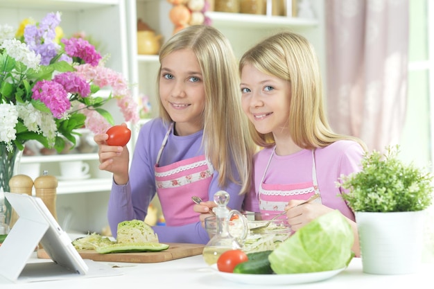 Zwei Mädchen in rosa Schürzen bereiten frischen Salat zu