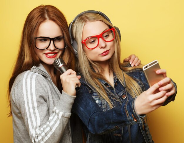 Zwei Mädchen mit einem Mikrofon, die zusammen singen und Spaß haben, machen Selfie