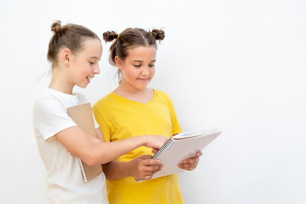 Zwei Mädchen mit Lehrbuch auf dem weißen Hintergrund. Teenager-Shows in einem Buch