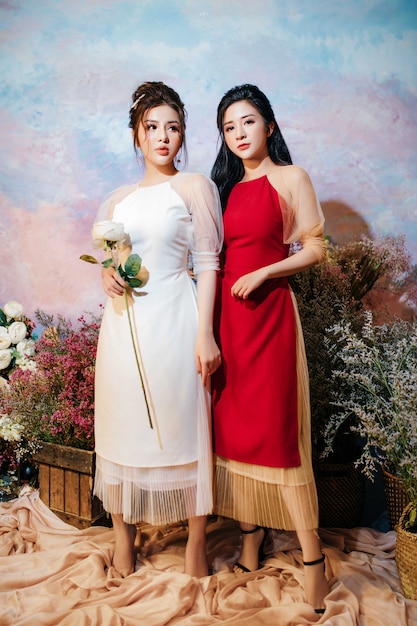 zwei Mädchen mit roten und weißen Kleidern stehen mit Blumen