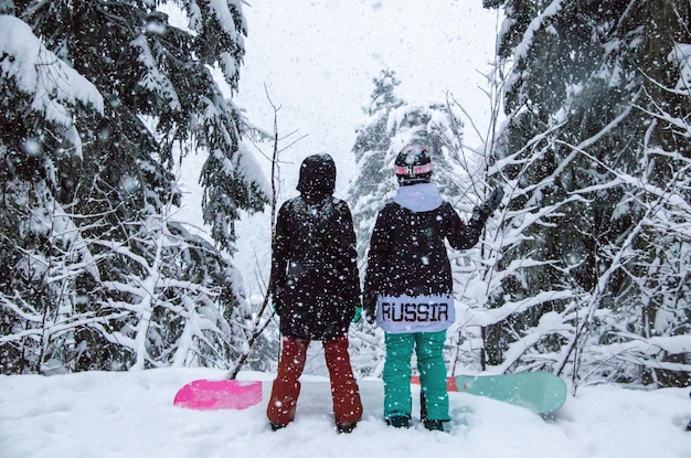 Zwei Mädchen mit Snowboards im Wald in den Bergen und im Schneefall