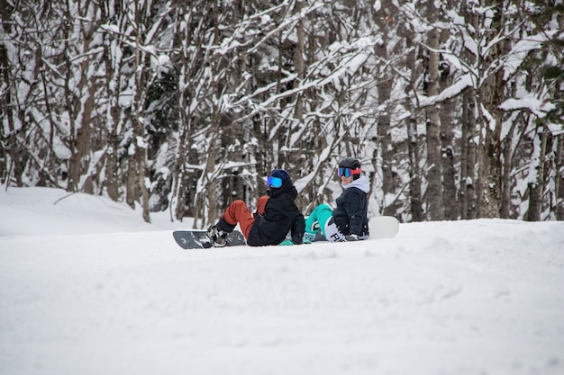 Zwei Mädchen mit Snowboards sitzen am Berghang
