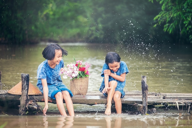 Zwei Mädchenkinder, die zusammen Wasser auf Holzbrücke über Sumpf, asiatisches ki sitzen und spielen