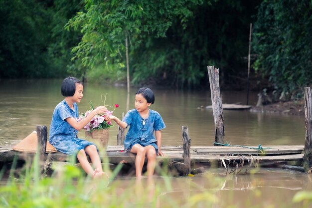 Zwei Mädchenkinder, die zusammen Wasser auf Holzbrücke über Sumpf sitzen und spielen