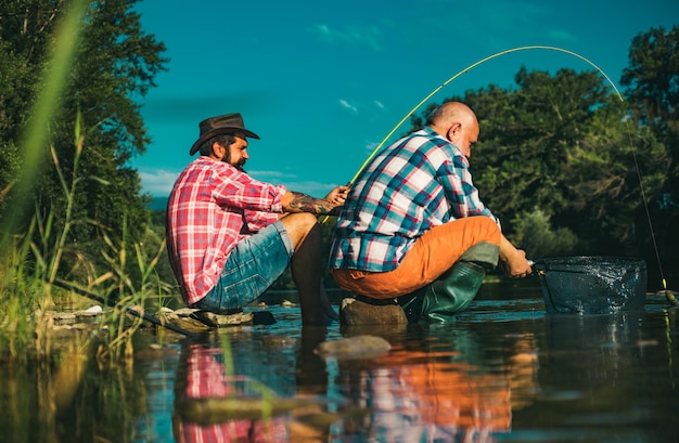 Zwei Männer, Freunde, Fischer, die am Fluss angeln, alter Vater und Sohn mit Stange am Fluss, Freizeitaktivität
