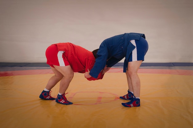 Zwei Männer in blauen und roten Strumpfhosen ringen auf einem gelben Tatami Sambo-Wrestler trainieren Sambo-Wettkampf