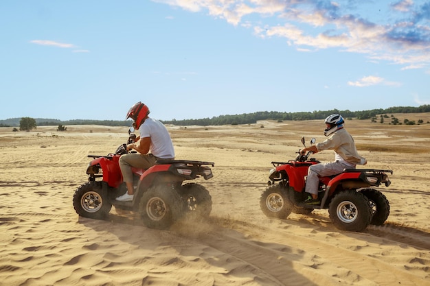 Zwei männer in helmen fahren auf einem atv in der wüste. männliche personen auf quads, sandrennen, dünensafari an heißen sonnigen tagen, 4x4 extremes abenteuer, quadfahren