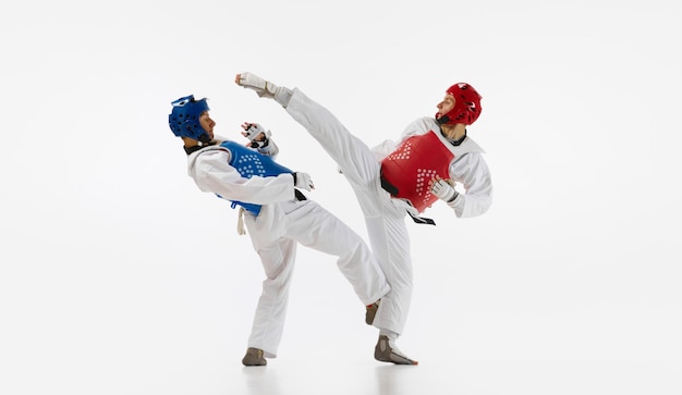 Foto zwei männer in kimono und helmen, die taekwondo-training üben, kämpfen isoliert auf weißem hintergrund