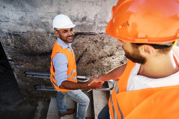 Zwei Männer Ingenieure in Arbeitskleidung Händeschütteln gegen Baustelle