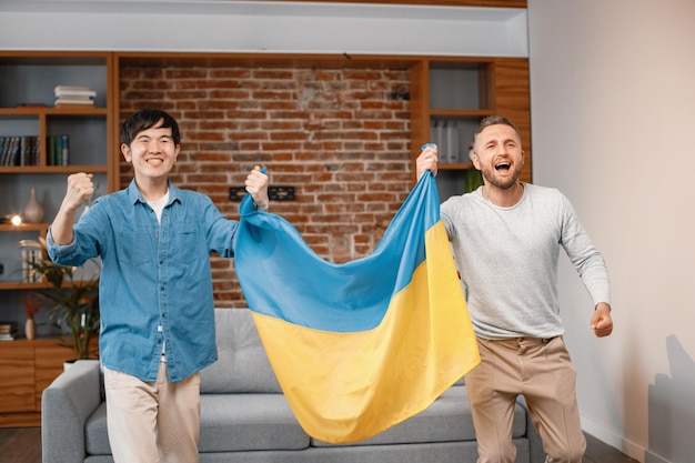 Zwei Männer schauen sich ein Fußballspiel im Fernsehen an und halten eine große Flagge der Ukraine