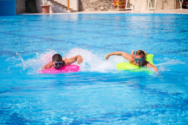 Zwei Männer schwimmen im Pool und schweben auf aufblasbaren Matratzen und entspannen sich