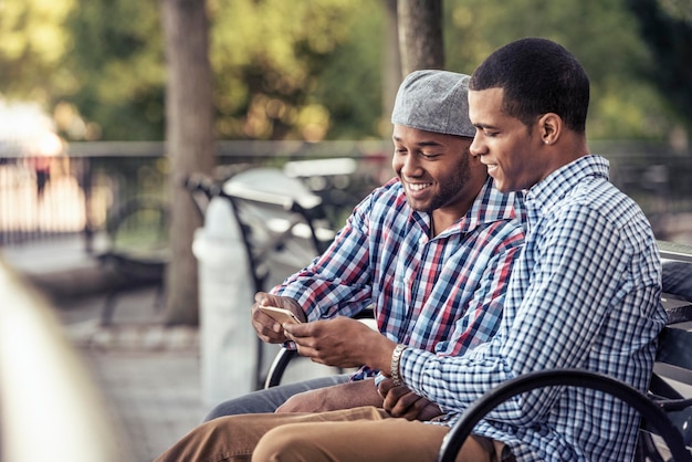 Zwei Männer sitzen in einem Park und schauen auf ein Smartphone