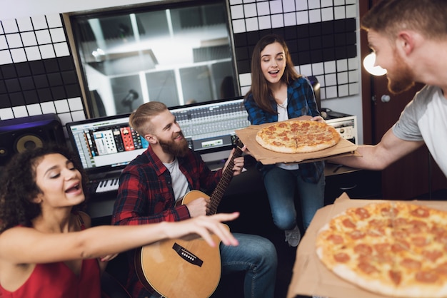 Zwei Männer und zwei Frauen im Tonstudio essen Pizza.