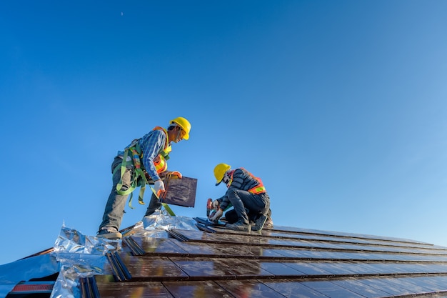 Zwei männliche Arbeiter in Sicherheitskleidung Installation des Dachziegelhauses Das ist ein Keramikziegeldach Auf der Baustelle