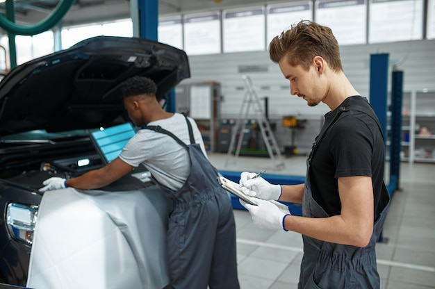 Zwei männliche Arbeiter reparieren Motor, Autoservice