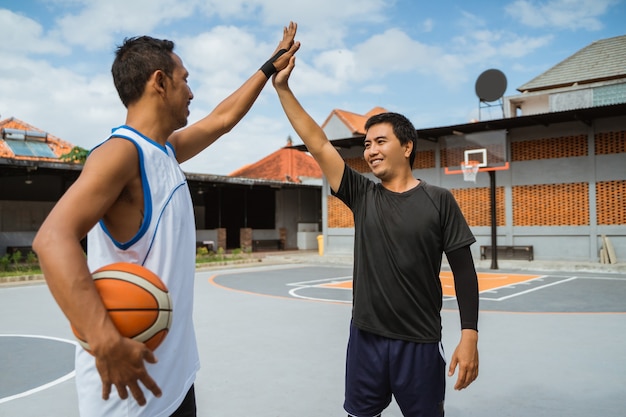 Zwei männliche Basketballspieler mit High Fives in der Pause beim Basketballspielen