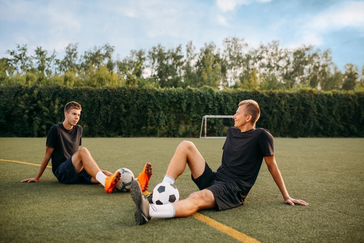 Foto zwei männliche fußballspieler ruhen auf dem rasen auf dem feld. fußballer im außenstadion, training vor dem spiel, fußballtraining